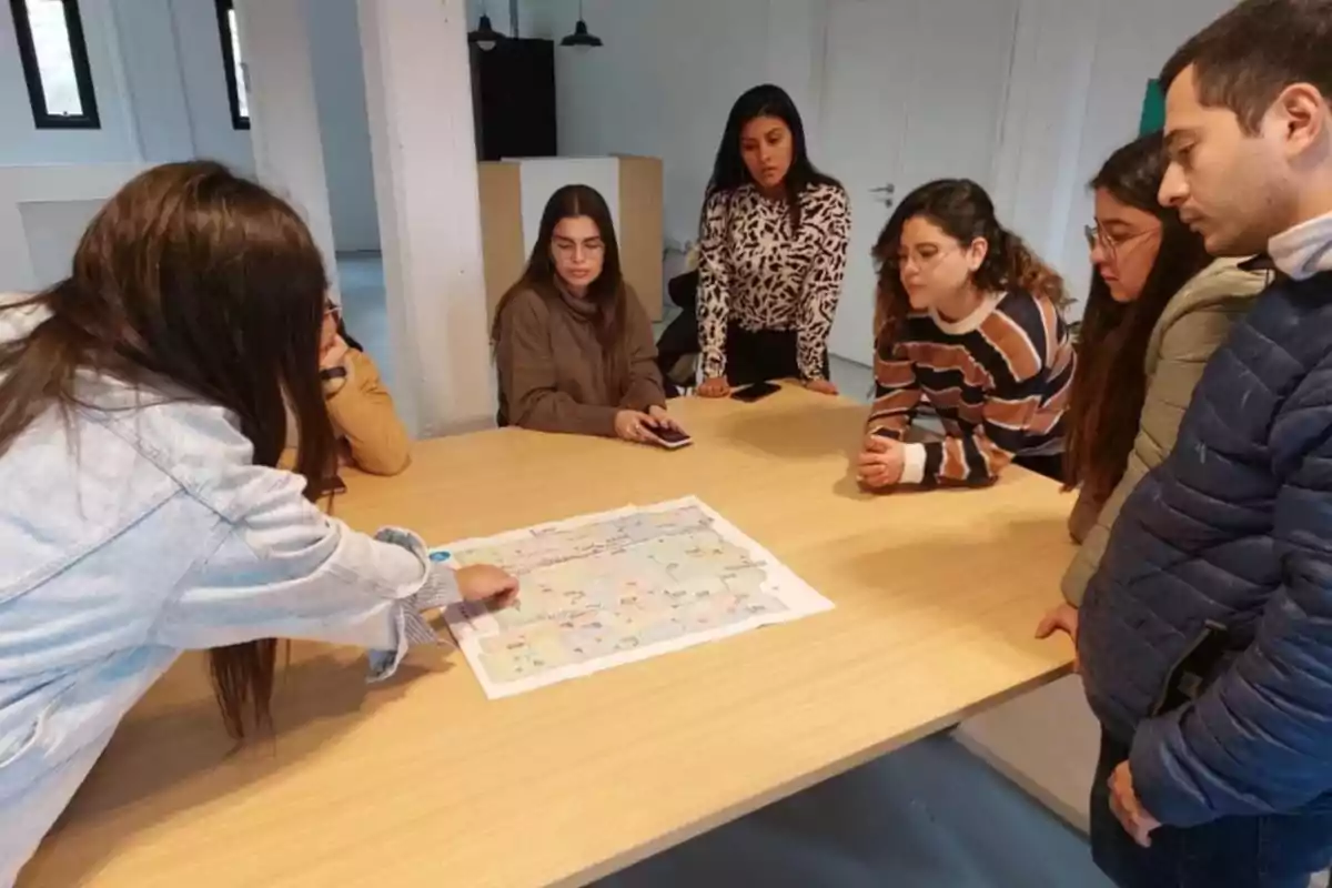 Un grupo de personas observa y analiza un mapa sobre una mesa en una sala de reuniones. Un grupo de personas observa y analiza un mapa sobre una mesa en una sala de reuniones.
