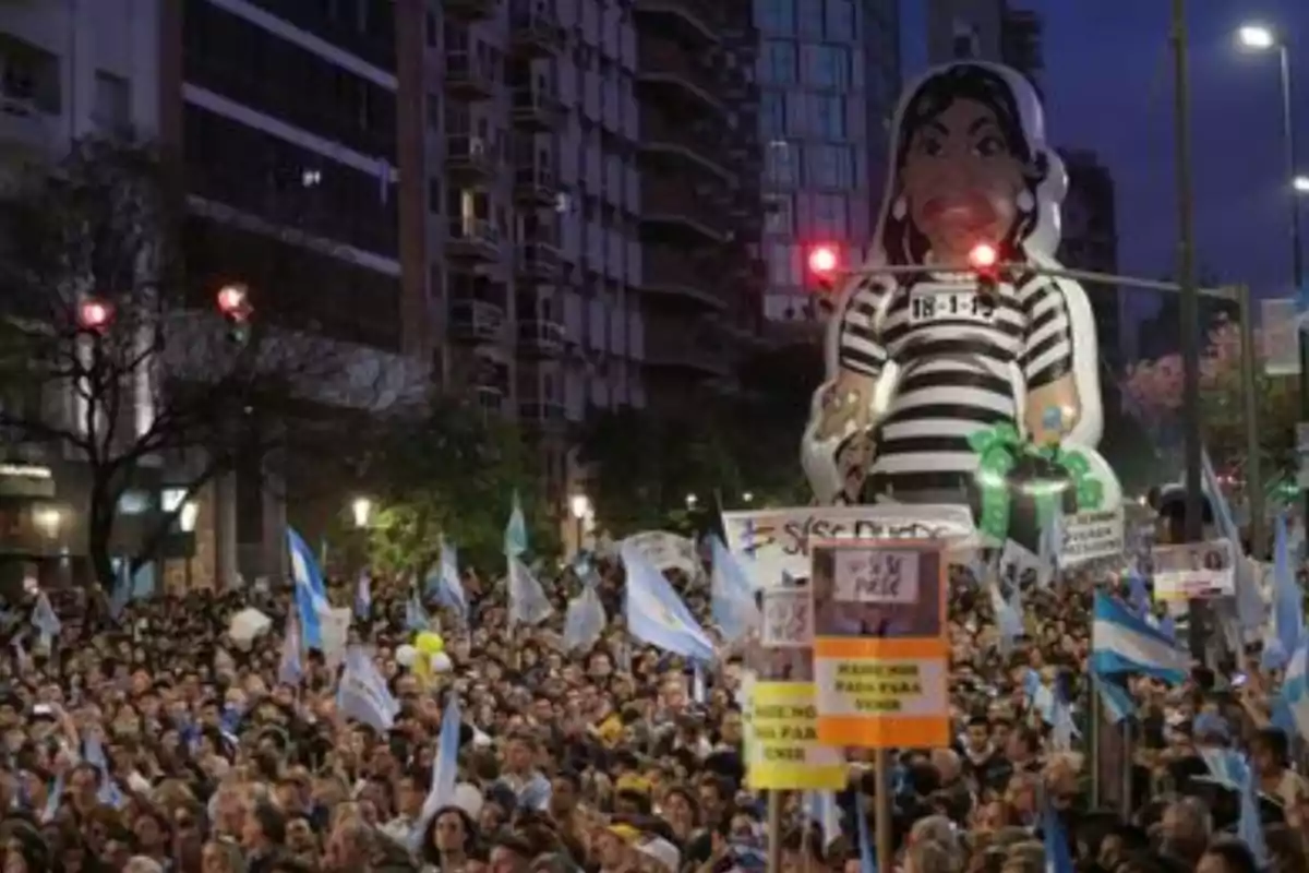Crowds of people marching down an avenue with Argentine flags and signs, alongside a large inflatable doll of a woman dressed in a prison uniform. Crowds of people marching down an avenue with Argentine flags and signs, alongside a large inflatable doll of a woman dressed in a prison uniform.