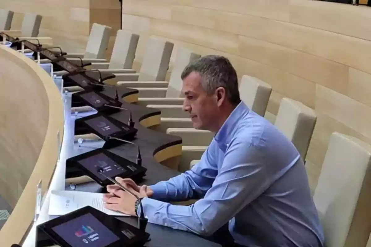 Man sitting in a modern conference room with several screens and microphones in front of him Man sitting in a modern conference room with several screens and microphones in front of him