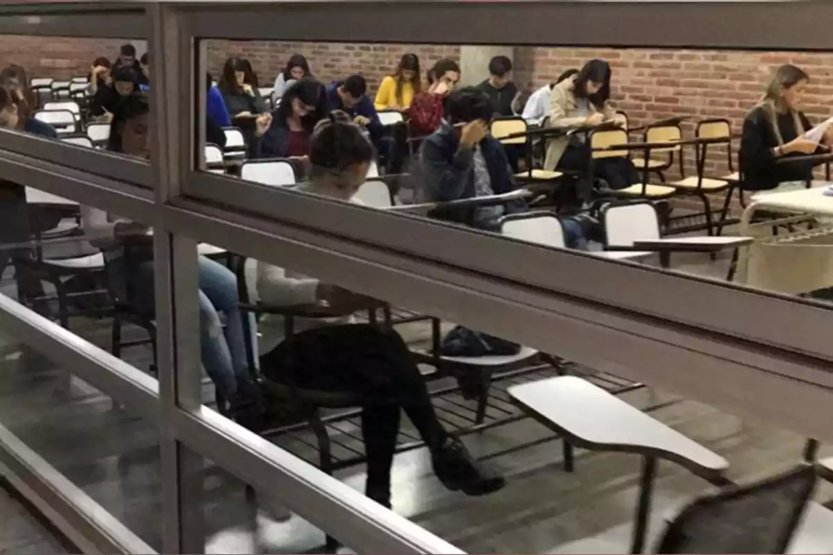 Students sitting at desks inside a classroom taking an exam while a person at the front appears to be supervising Students sitting at desks inside a classroom taking an exam while a person at the front appears to be supervising