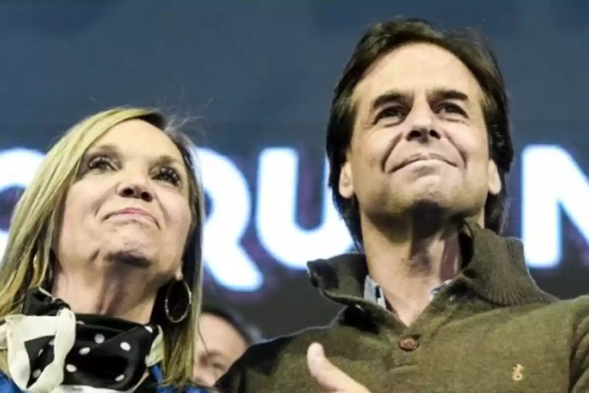 Una mujer y un hombre miran hacia adelante con expresiones de orgullo y satisfacción en un ambiente iluminado