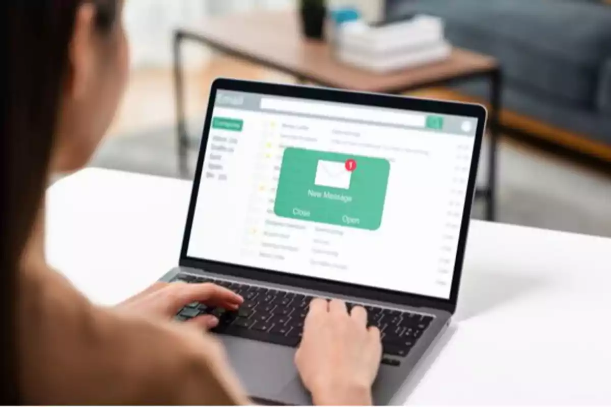 Persona revisando su correo electrónico en una laptop con una notificación de nuevo mensaje en la pantalla Persona revisando su correo electrónico en una laptop con una notificación de nuevo mensaje en la pantalla