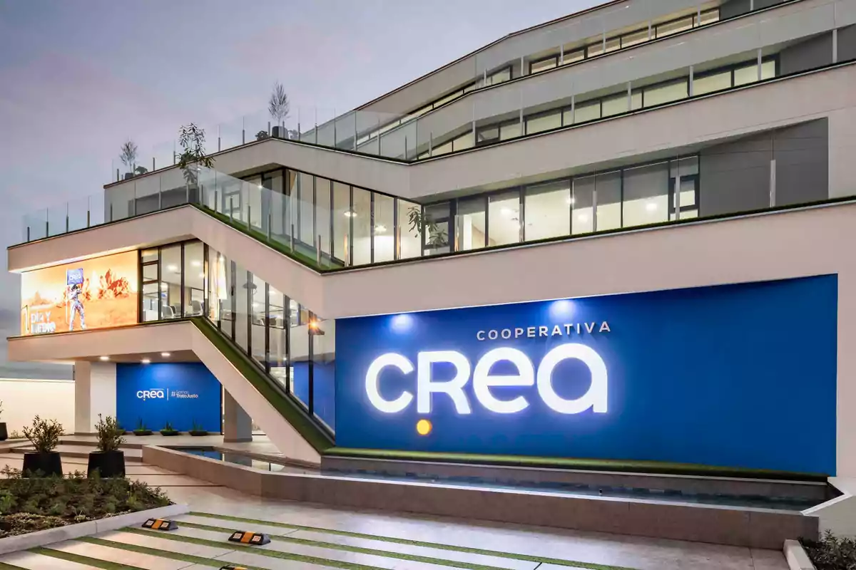 Edificio moderno de varios niveles con fachada de vidrio y un gran letrero azul que dice Cooperativa CREA iluminado en la entrada