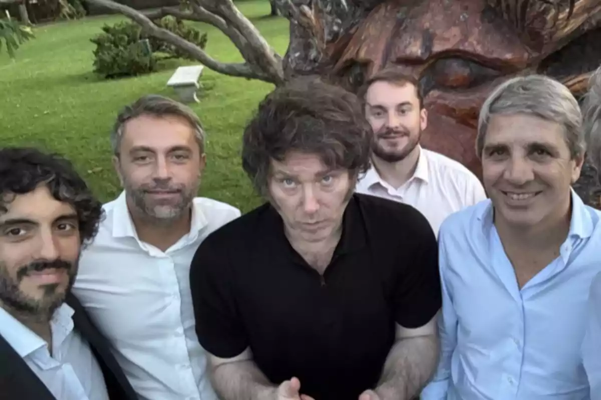 Five men pose for a selfie outdoors with grass and a tree in the background. Five men pose for a selfie outdoors with grass and a tree in the background.