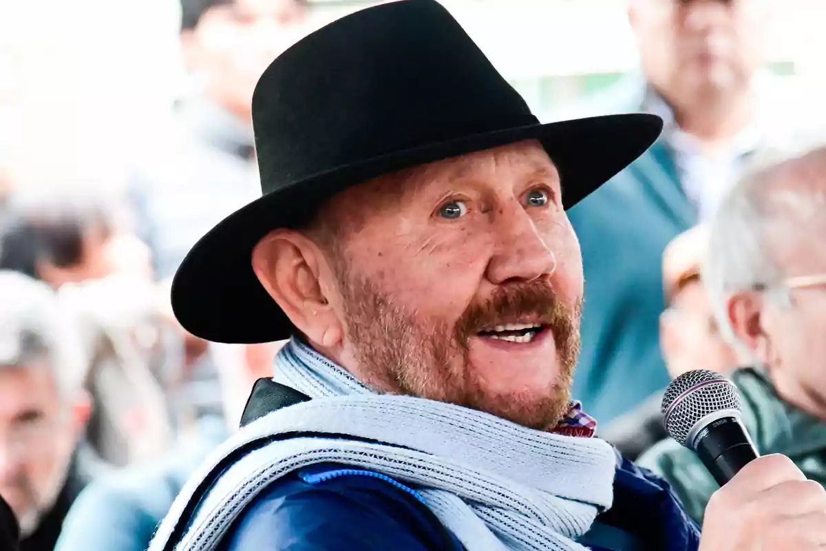 Hombre de barba y sombrero negro hablando por un micrófono en un evento público Hombre de barba y sombrero negro hablando por un micrófono en un evento público