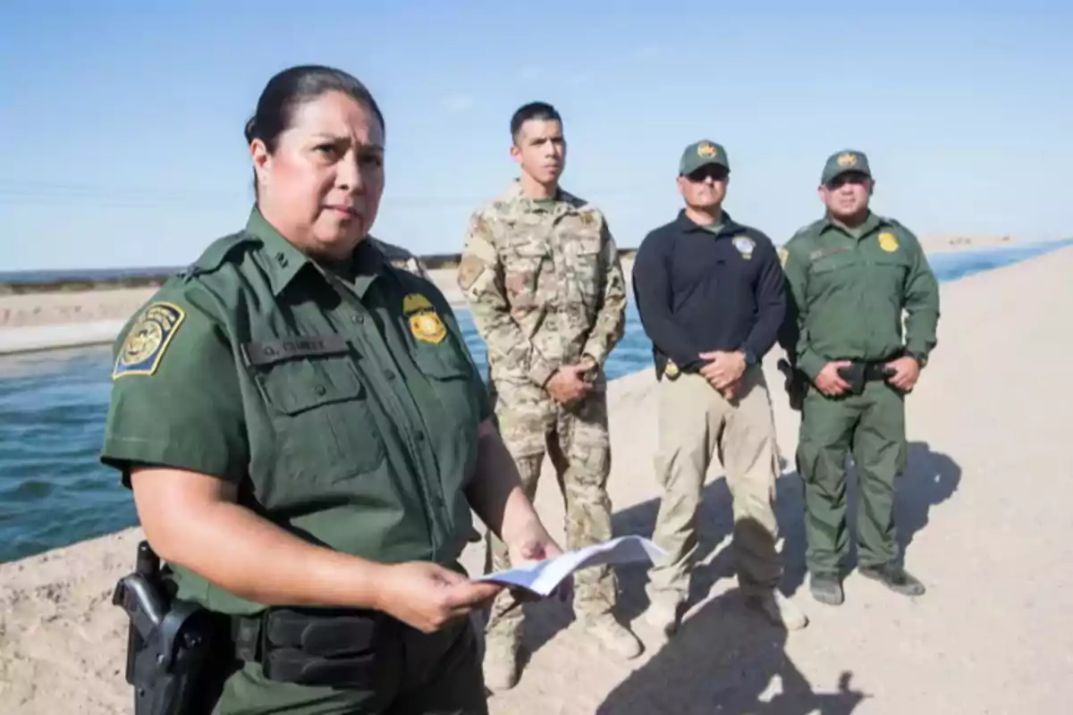 Cuatro agentes de seguridad, dos de ellos con uniforme verde, uno con uniforme militar y otro con ropa táctica, están de pie junto a un canal de agua en un entorno desértico bajo un cielo despejado Cuatro agentes de seguridad, dos de ellos con uniforme verde, uno con uniforme militar y otro con ropa táctica, están de pie junto a un canal de agua en un entorno desértico bajo un cielo despejado