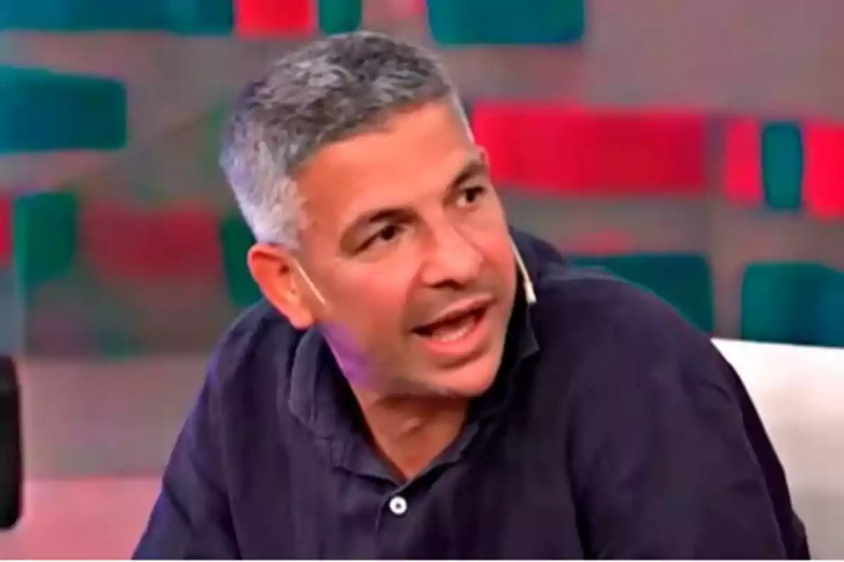 Short-haired, gray-haired man speaking on a television show with a colorful background Short-haired, gray-haired man speaking on a television show with a colorful background