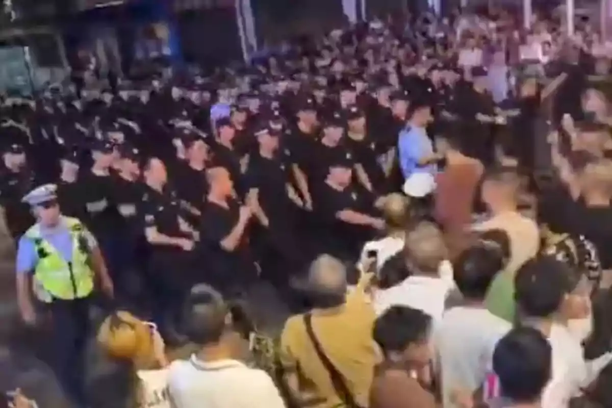 A large group of police officers moves through a crowd of people on a street at night.