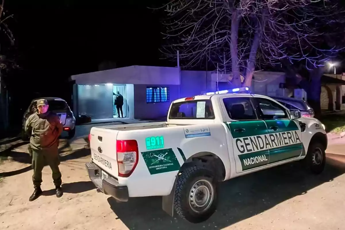 Patrulla de la Gendarmería Nacional Argentina estacionada frente a una casa durante la noche con un agente de pie y luces encendidas en la camioneta