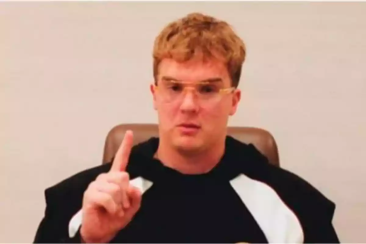 Young man with glasses and a black sweatjersey raising his index finger while sitting on a chair Young man with glasses and a black sweatjersey raising his index finger while sitting on a chair