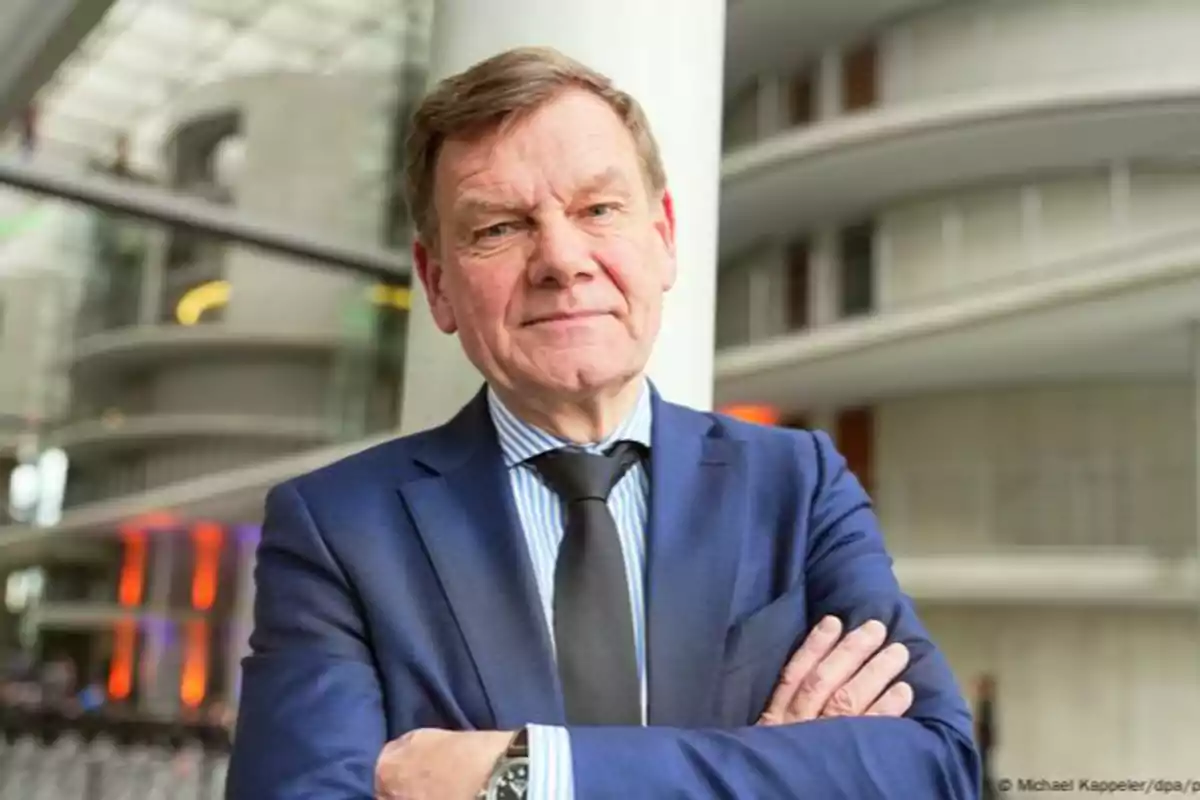 Middle-aged man in a blue suit and black tie posing with his arms crossed in a modern office environment. Middle-aged man in a blue suit and black tie posing with his arms crossed in a modern office environment.