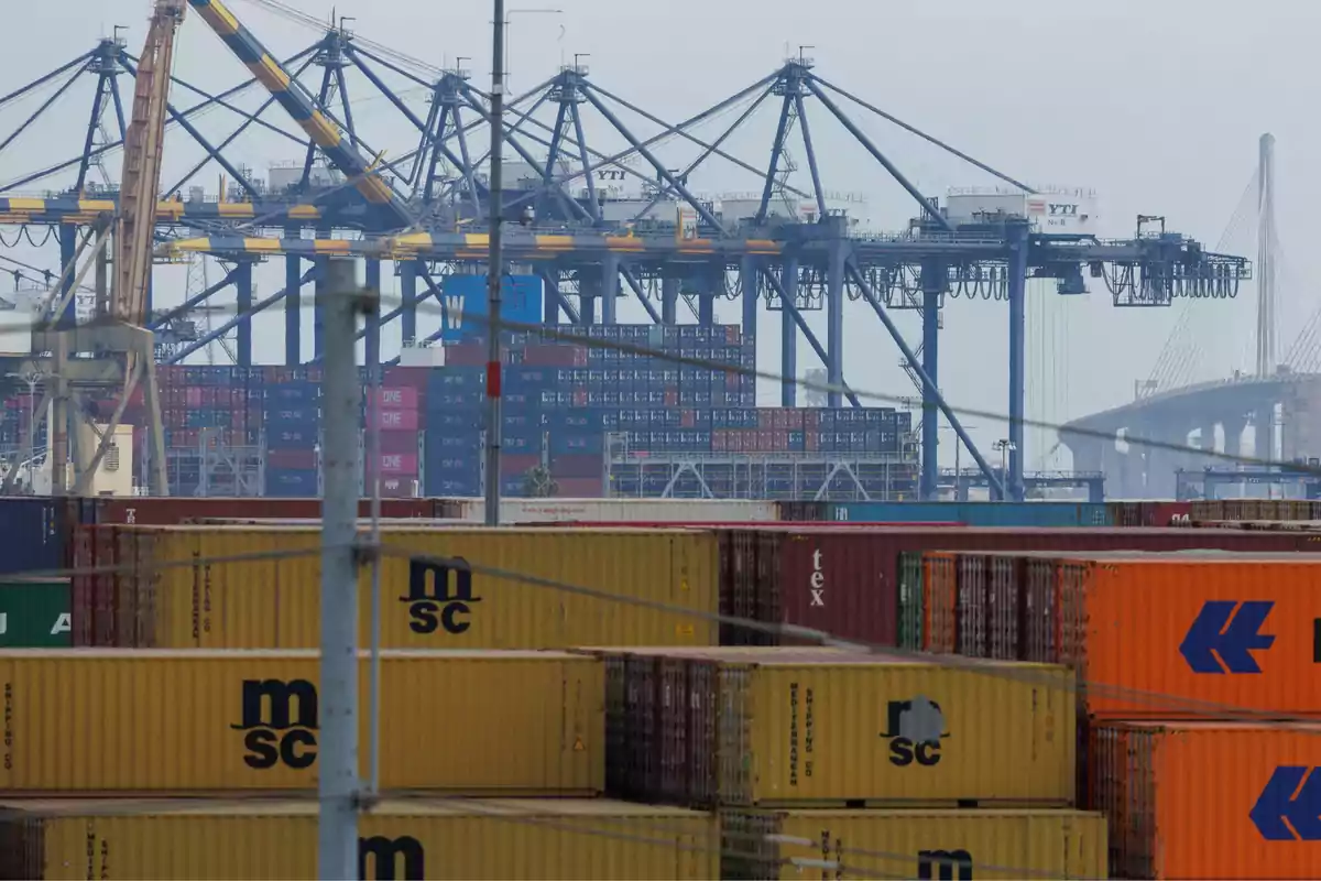 Contenedores apilados en un puerto industrial con grúas y un puente al fondo Contenedores apilados en un puerto industrial con grúas y un puente al fondo