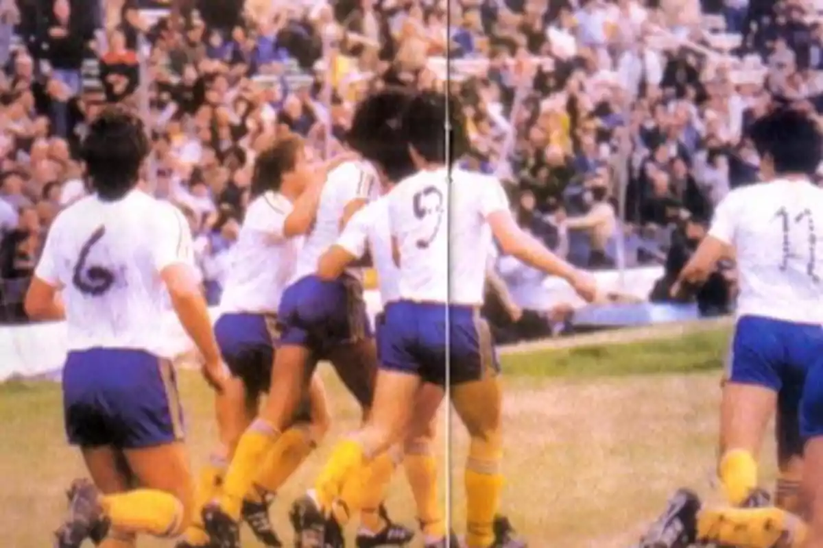 Soccer players in white and blue uniforms celebrate a goal in a stadium full of fans. Soccer players in white and blue uniforms celebrate a goal in a stadium full of fans.