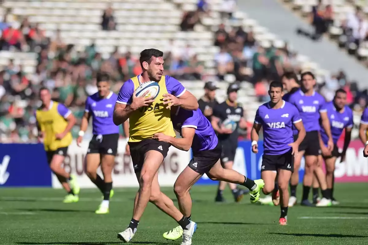 Rugby players training in a stadium while one of them runs with the ball and another tries to stop him. Rugby players training in a stadium while one of them runs with the ball and another tries to stop him.