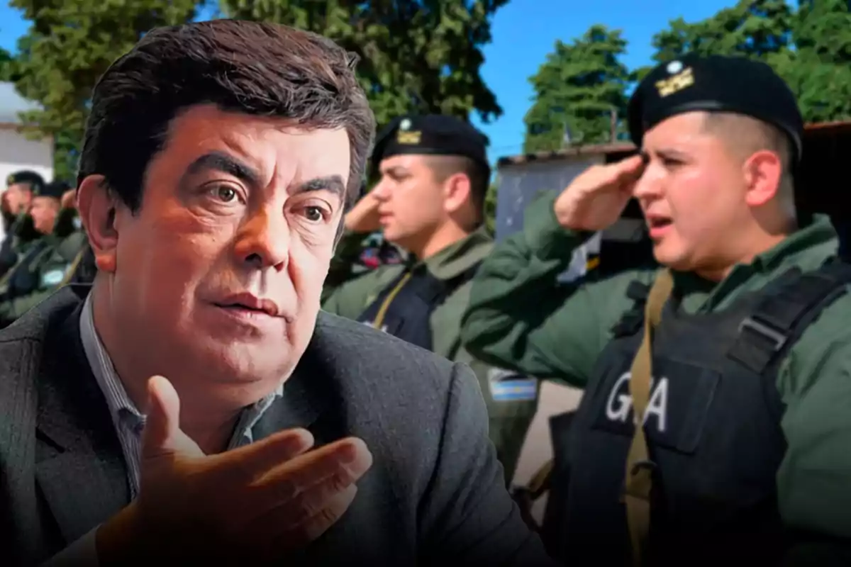 Un hombre de cabello oscuro y expresión seria en primer plano con un grupo de agentes uniformados al fondo uno de ellos saludando militarmente