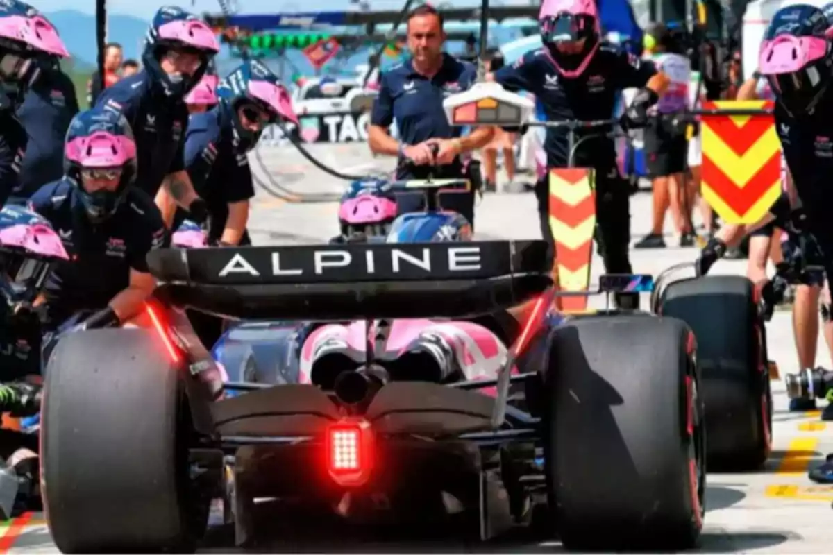 Un auto de Fórmula 1 del equipo Alpine realiza una parada en boxes mientras varios mecánicos con cascos rosas trabajan a su alrededor Un auto de Fórmula 1 del equipo Alpine realiza una parada en boxes mientras varios mecánicos con cascos rosas trabajan a su alrededor