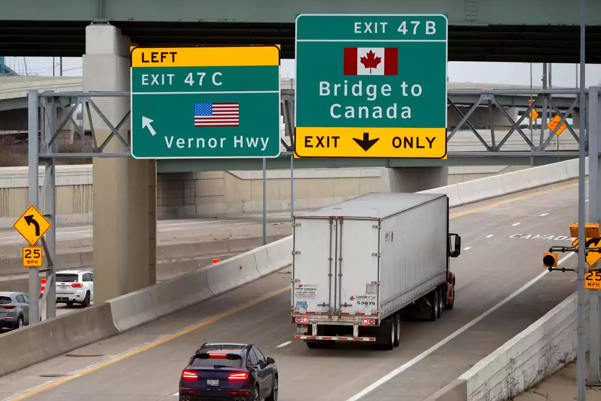 Un camión y un automóvil circulan por una autopista con señales que indican la salida hacia Canadá y la autopista Vernor en Estados Unidos. Un camión y un automóvil circulan por una autopista con señales que indican la salida hacia Canadá y la autopista Vernor en Estados Unidos.