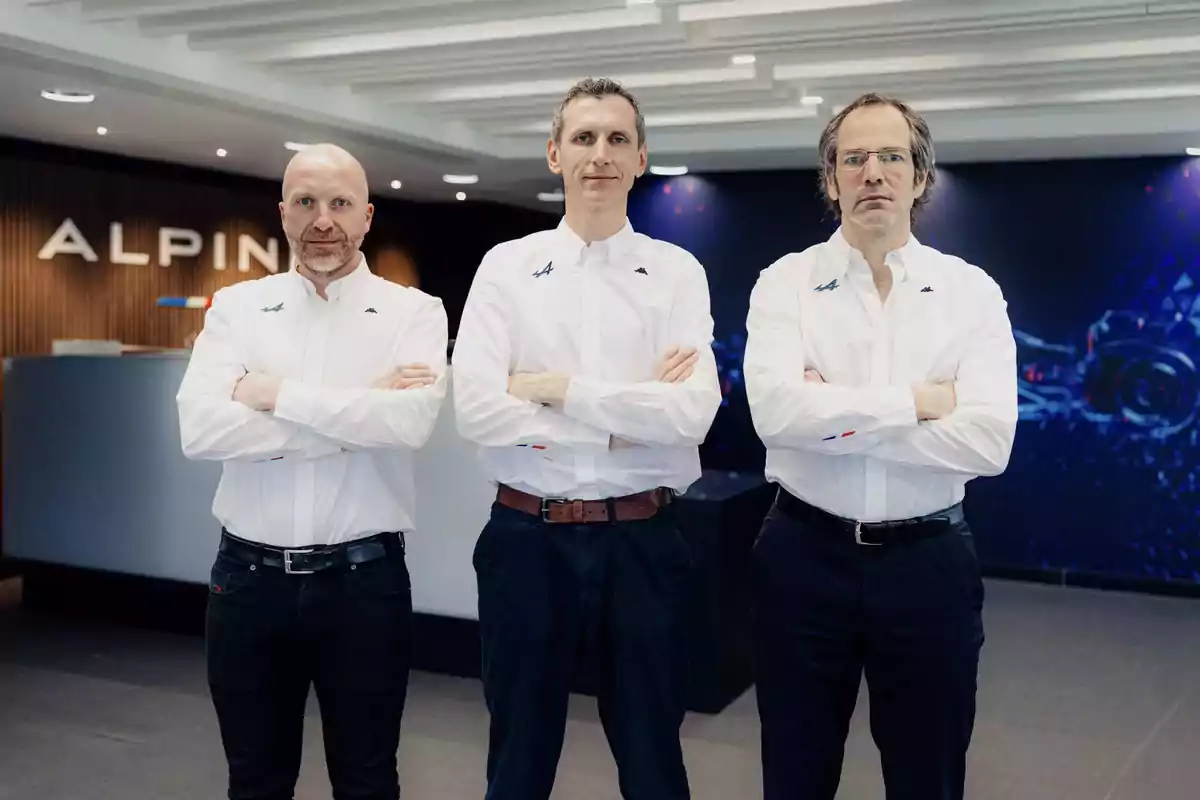 Tres hombres con camisas blancas y brazos cruzados posan en una oficina moderna con el logo de Alpine al fondo Tres hombres con camisas blancas y brazos cruzados posan en una oficina moderna con el logo de Alpine al fondo