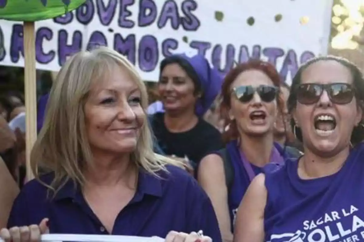 Women participating in a feminist demonstration with purple jerseys and banners as they march and chant slogans