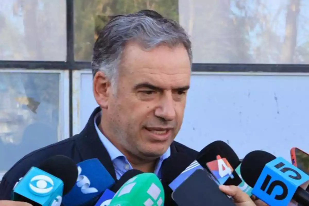 Gray-haired man speaking in front of several microphones from different media outlets Gray-haired man speaking in front of several microphones from different media outlets