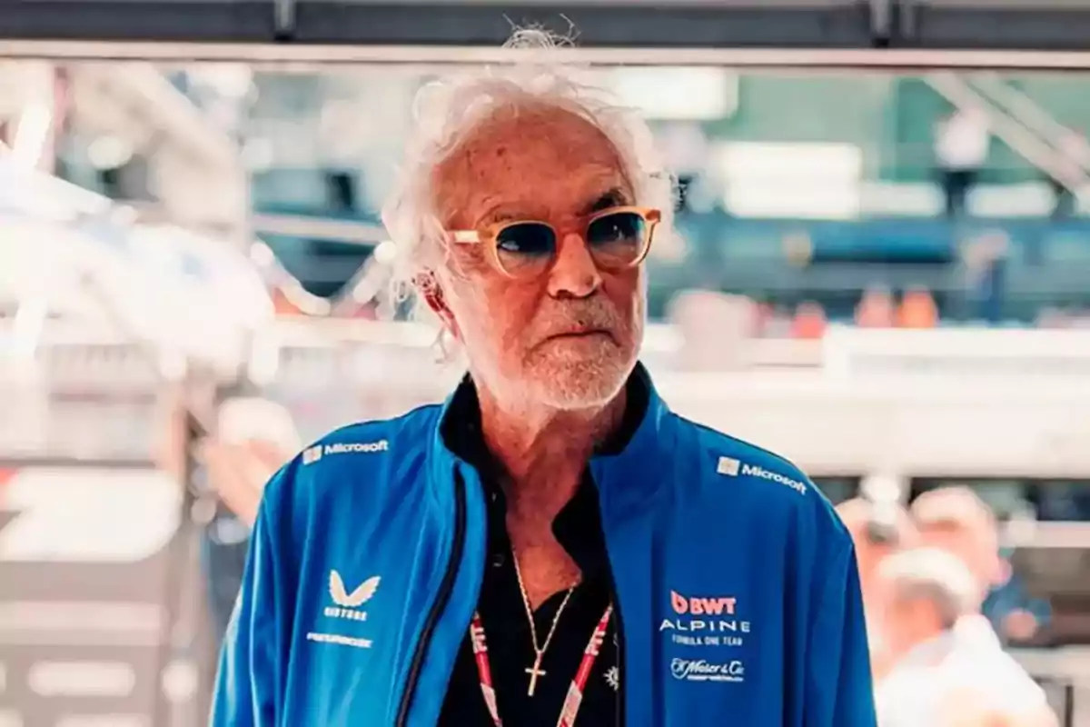 Hombre mayor con gafas de sol y chaqueta azul de Alpine en un entorno de carreras