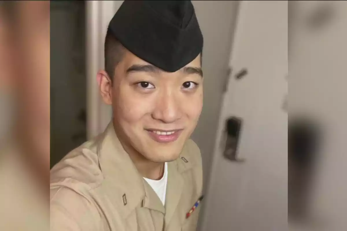 Young man in a beige military uniform and black cap smiling in front of the camera indoors Young man in a beige military uniform and black cap smiling in front of the camera indoors