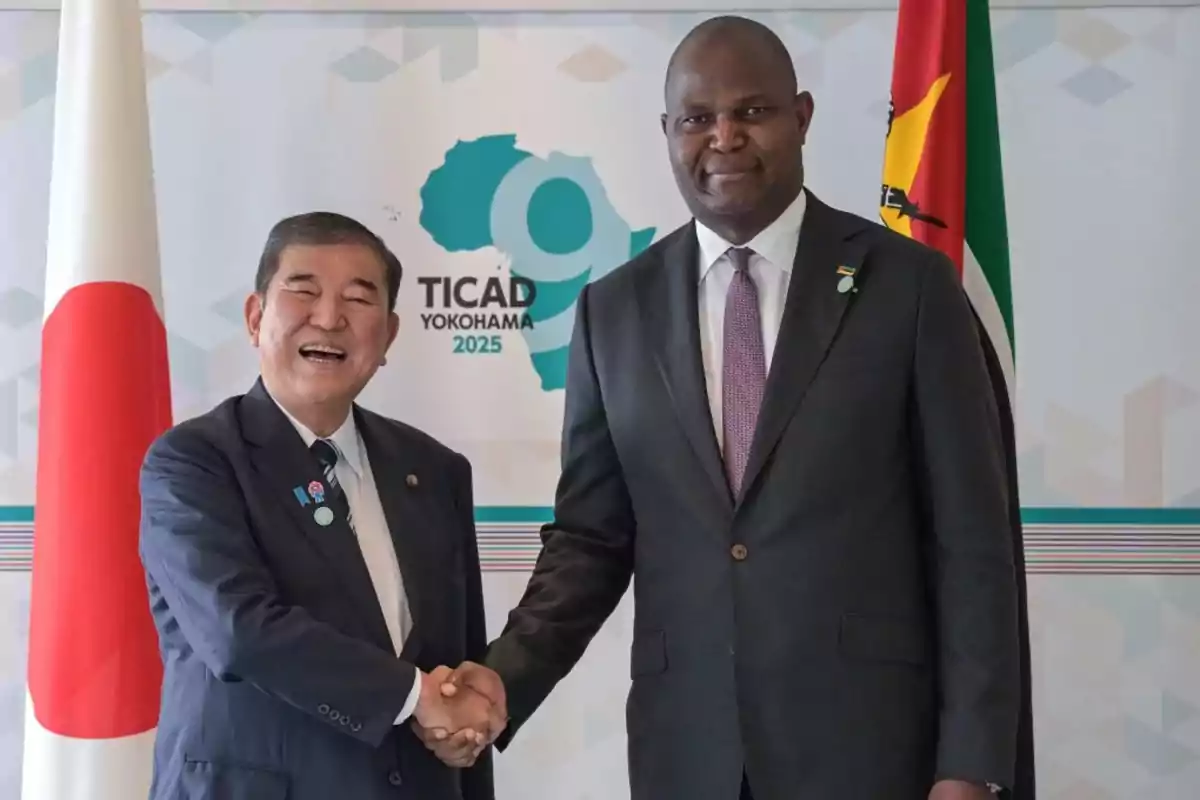 Two men in suits shake hands in front of a TICAD Yokohama 2025 conference sign with the flags of Japan and Mozambique on either side. Two men in suits shake hands in front of a TICAD Yokohama 2025 conference sign with the flags of Japan and Mozambique on either side.