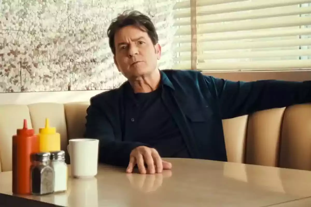 Hombre sentado en una mesa de cafetería con botellas de condimentos y una taza blanca sobre la mesa Hombre sentado en una mesa de cafetería con botellas de condimentos y una taza blanca sobre la mesa