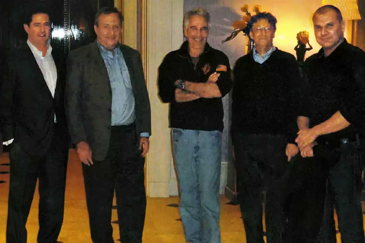 Five men pose together in an elegant room with background decor and warm lighting.