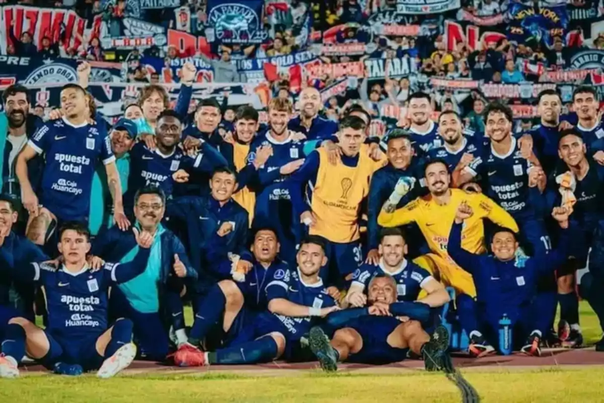 Jugadores de un equipo de fútbol celebran juntos en la cancha con aficionados y banderas en las gradas al fondo