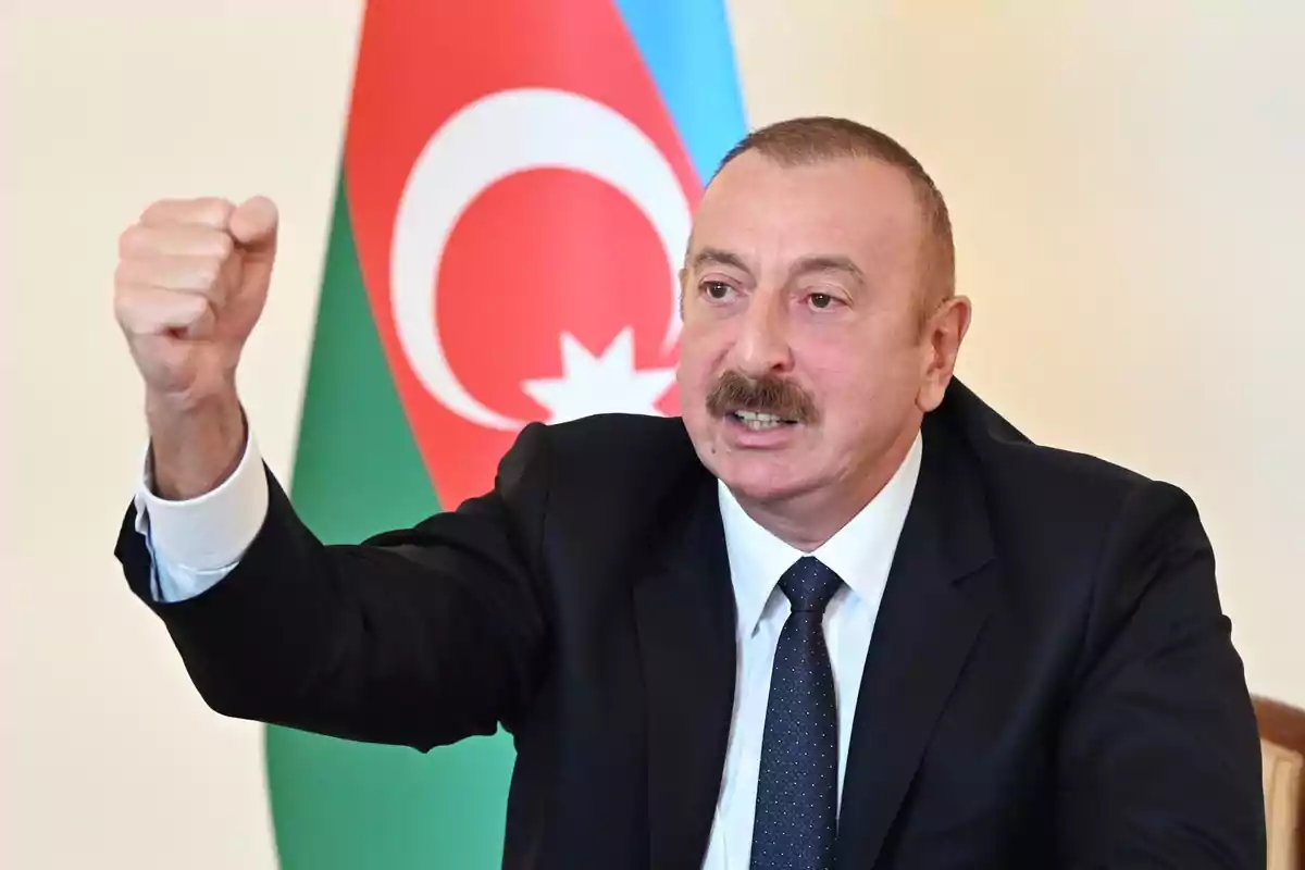 Hombre de traje oscuro levantando el puño frente a una bandera de Azerbaiyán