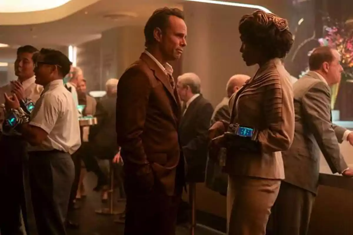 Two elegantly dressed people are talking at a bar with a sophisticated atmosphere and several people in the background. Two elegantly dressed people are talking at a bar with a sophisticated atmosphere and several people in the background.