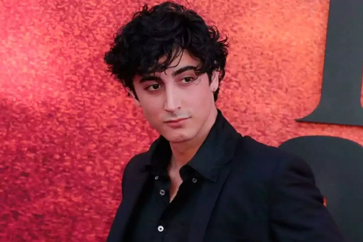 Young man with dark curly hair wearing a jersey and black jacket posing in front of a red background Young man with dark curly hair wearing a jersey and black jacket posing in front of a red background