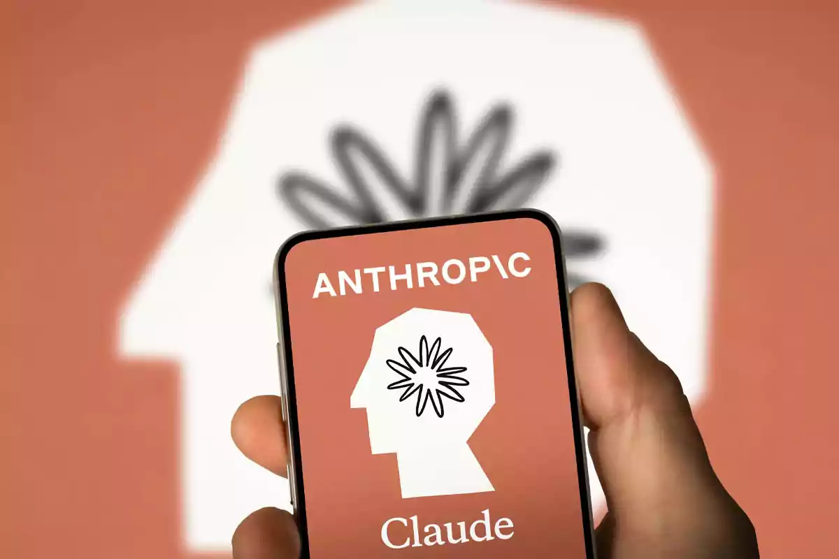 Person holding a mobile phone displaying the Anthropic Claude logo against a background of the same logo in orange. Person holding a mobile phone displaying the Anthropic Claude logo against a background of the same logo in orange.
