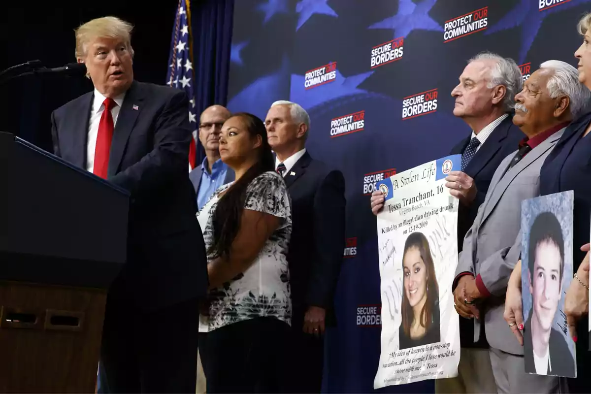 Donald Trump habla en un podio acompañado de varias personas, algunas de ellas sostienen carteles con fotografías de jóvenes y mensajes, mientras al fondo se ven letreros que dicen Secure Our Borders y Protect Our Communities Donald Trump habla en un podio acompañado de varias personas, algunas de ellas sostienen carteles con fotografías de jóvenes y mensajes, mientras al fondo se ven letreros que dicen Secure Our Borders y Protect Our Communities