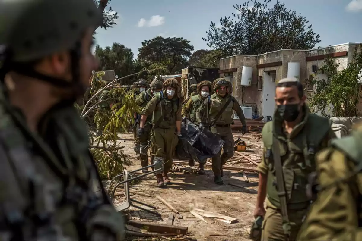 Soldiers wearing masks carry a stretcher through an area with debris and fallen trees in front of a damaged building. Soldiers wearing masks carry a stretcher through an area with debris and fallen trees in front of a damaged building.