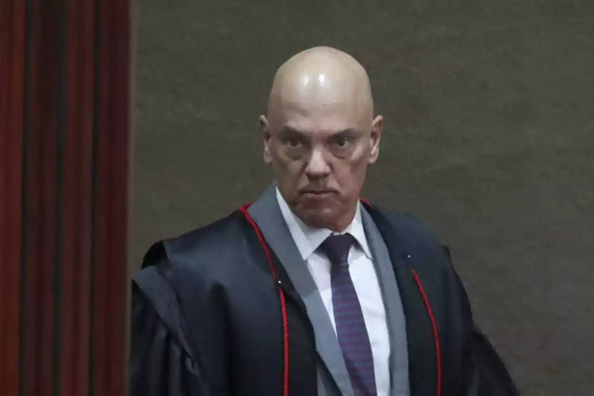 Bald man with a black robe and tie, serious expression, in a formal setting Bald man with a black robe and tie, serious expression, in a formal setting