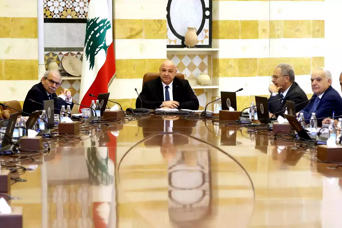 Cinco hombres con trajes formales sentados alrededor de una mesa de reuniones en una sala oficial con la bandera de Líbano al fondo