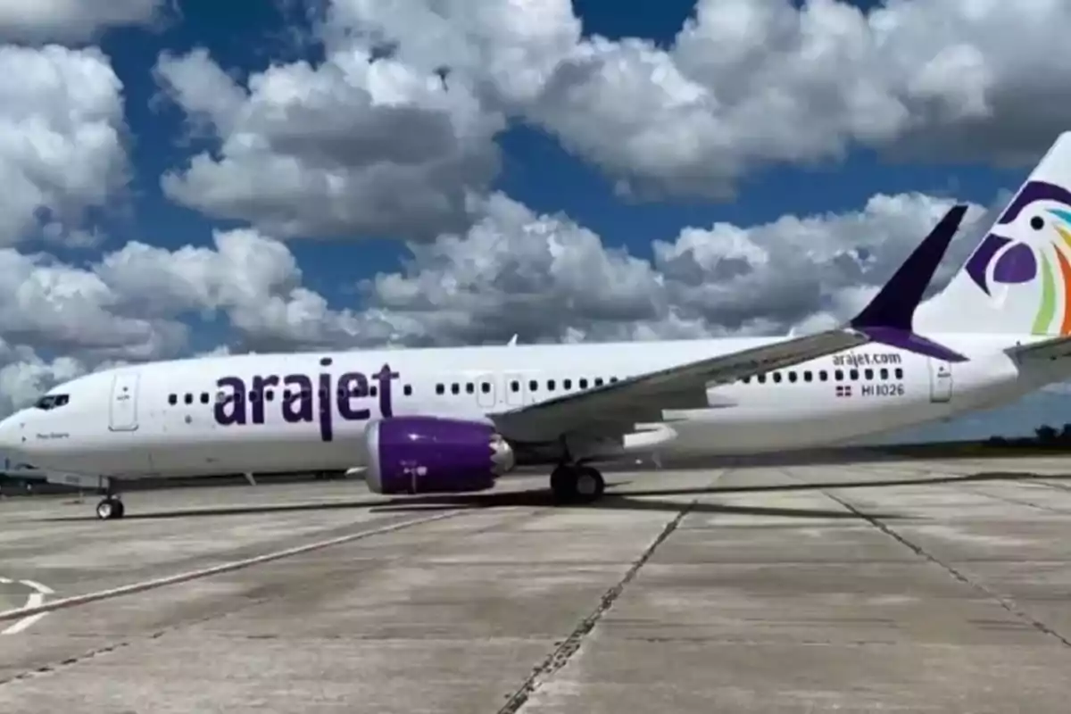 Avión de la aerolínea Arajet estacionado en una pista de aeropuerto bajo un cielo con nubes blancas