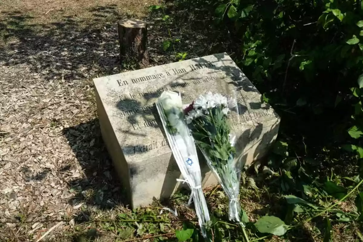 Ramo de flores blancas y moradas sobre una placa conmemorativa de piedra en un entorno natural