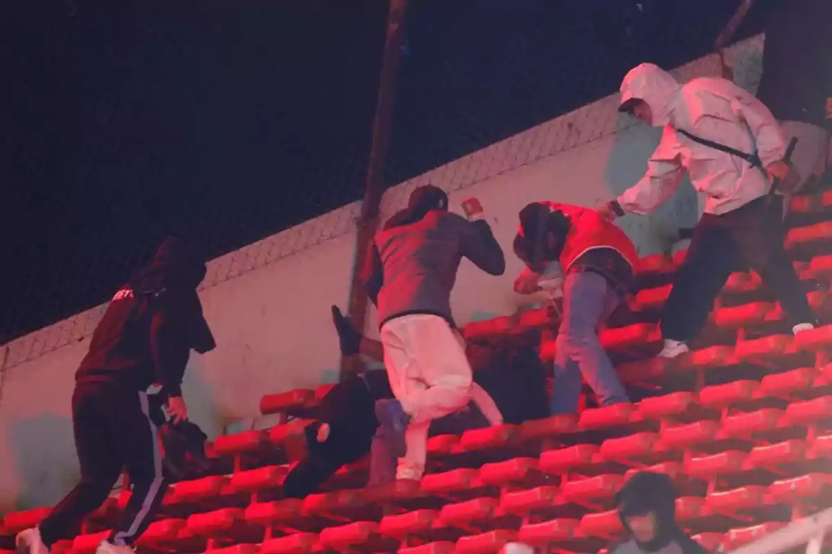 People fighting in the stands of a stadium lit with red lights