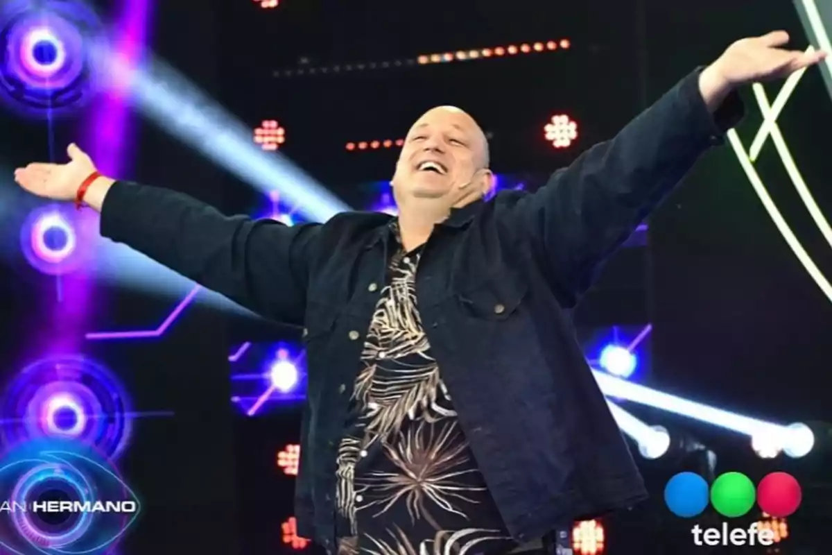 Smiling bald man with open arms on a colorful TV set with lights and the Telefe logo in the corner Smiling bald man with open arms on a colorful TV set with lights and the Telefe logo in the corner