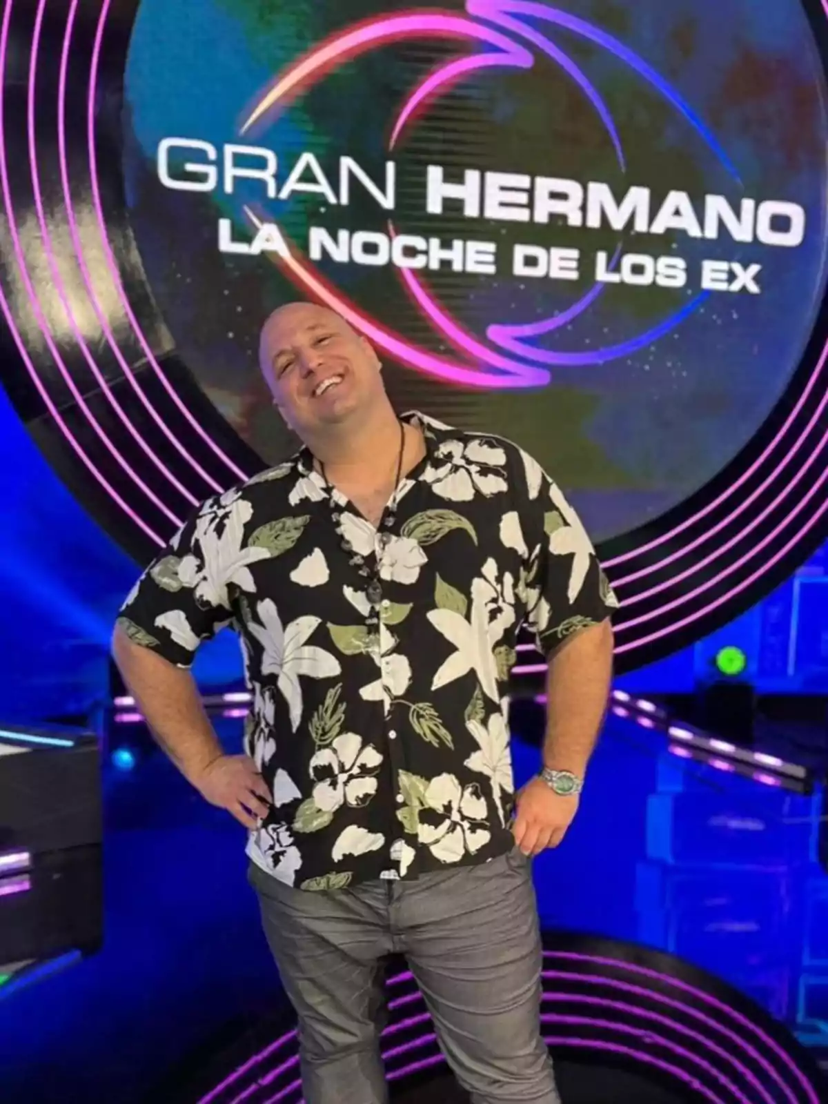 Smiling man in a floral jersey posing in front of a Big Brother: Night of the Exes sign on a set lit with neon lights Smiling man in a floral jersey posing in front of a Big Brother: Night of the Exes sign on a set lit with neon lights