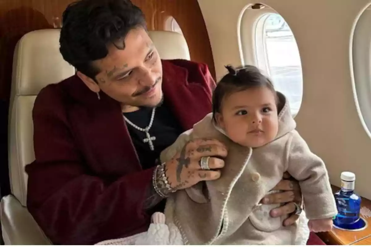 Hombre con chaqueta roja sosteniendo a un bebé con abrigo beige dentro de un avión privado