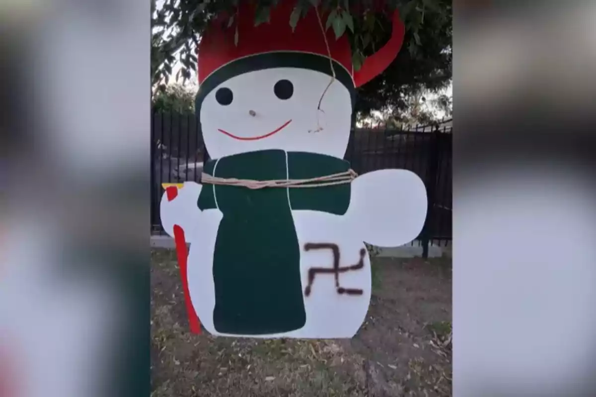 Muñeco de nieve decorativo con bufanda verde y gorro rojo, atado con una cuerda y con un símbolo pintado en el costado