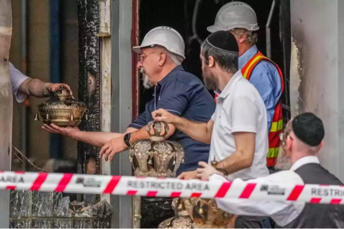 Varias personas con cascos y kipás recuperan objetos religiosos de un edificio quemado detrás de una cinta de área restringida Varias personas con cascos y kipás recuperan objetos religiosos de un edificio quemado detrás de una cinta de área restringida