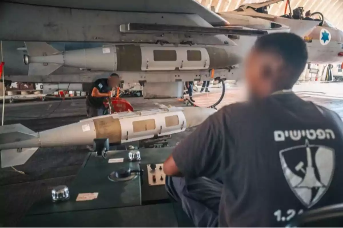 Military technicians prepare and inspect weaponry under the wing of a fighter jet in a hangar. Military technicians prepare and inspect weaponry under the wing of a fighter jet in a hangar.