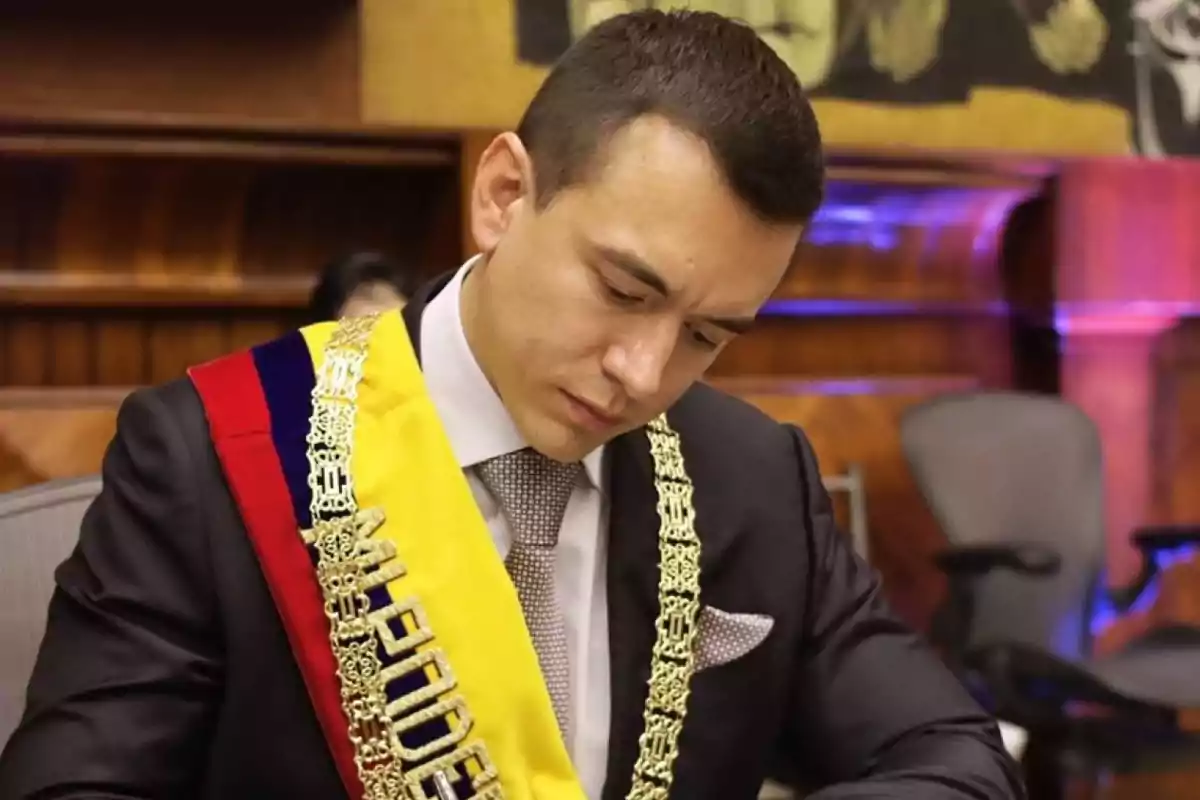 Hombre con banda presidencial y cadena dorada firmando un documento en un entorno formal