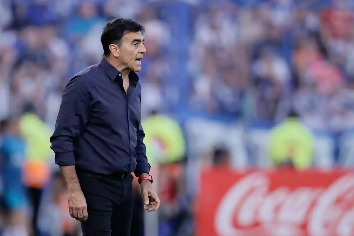 Entrenador de fútbol de pie en la cancha dando indicaciones durante un partido con el público desenfocado al fondo Entrenador de fútbol de pie en la cancha dando indicaciones durante un partido con el público desenfocado al fondo