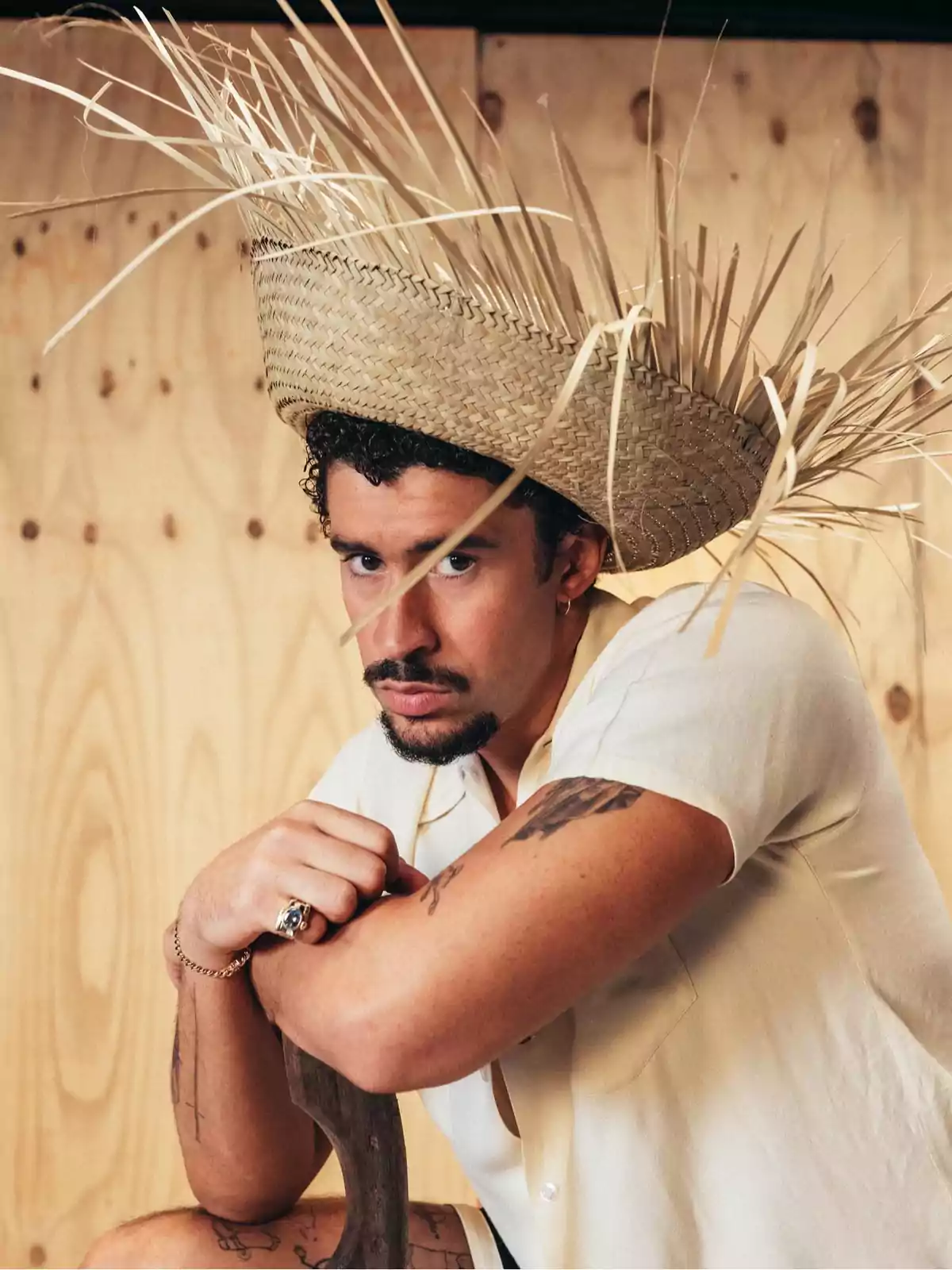 Hombre con sombrero de paja grande y camisa clara sentado frente a un fondo de madera Hombre con sombrero de paja grande y camisa clara sentado frente a un fondo de madera